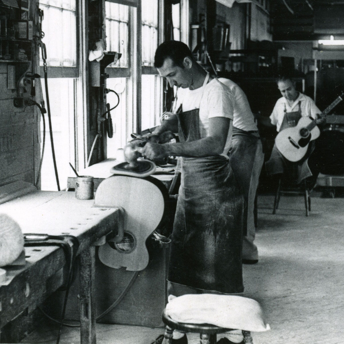Black and white photo of a worker polishing a guitar