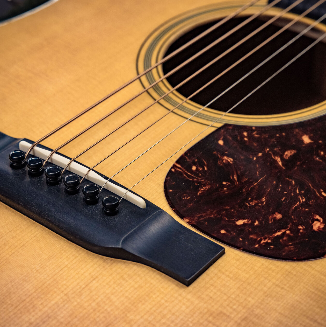 Acoustic guitar bridge, strings, soundhole, and pickguard