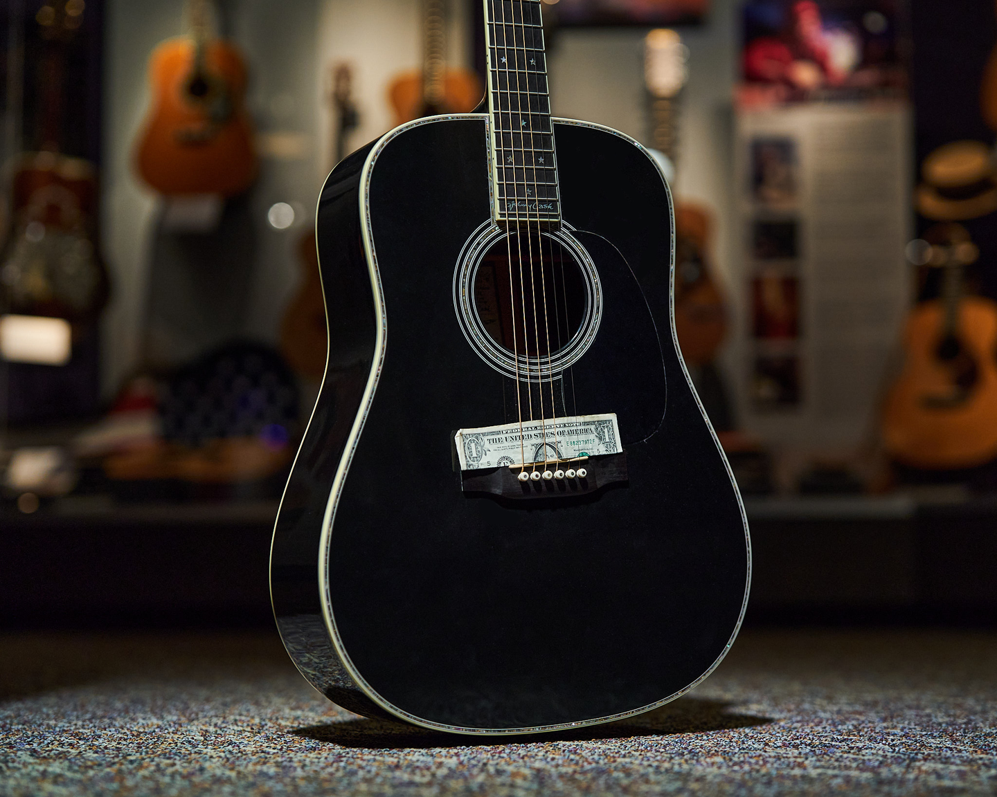 Photo of a black guitar with a dollar bill between the bridge and soundhole