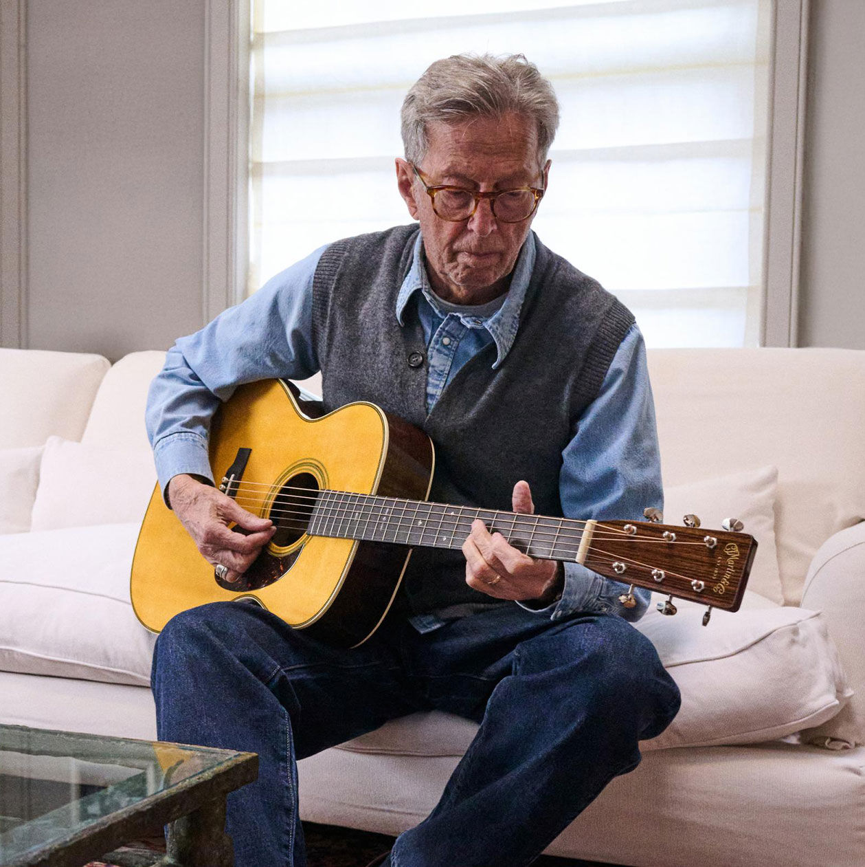 Eric Clapton playing an acoustic guitar on a couch