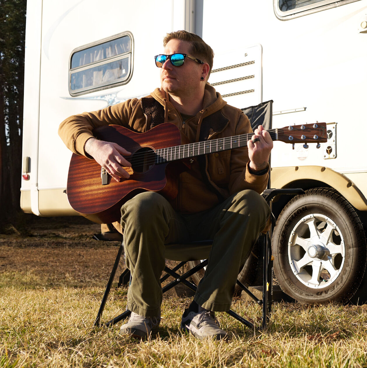 Person sitting outside playing an acoustic guitar in front of a trailer