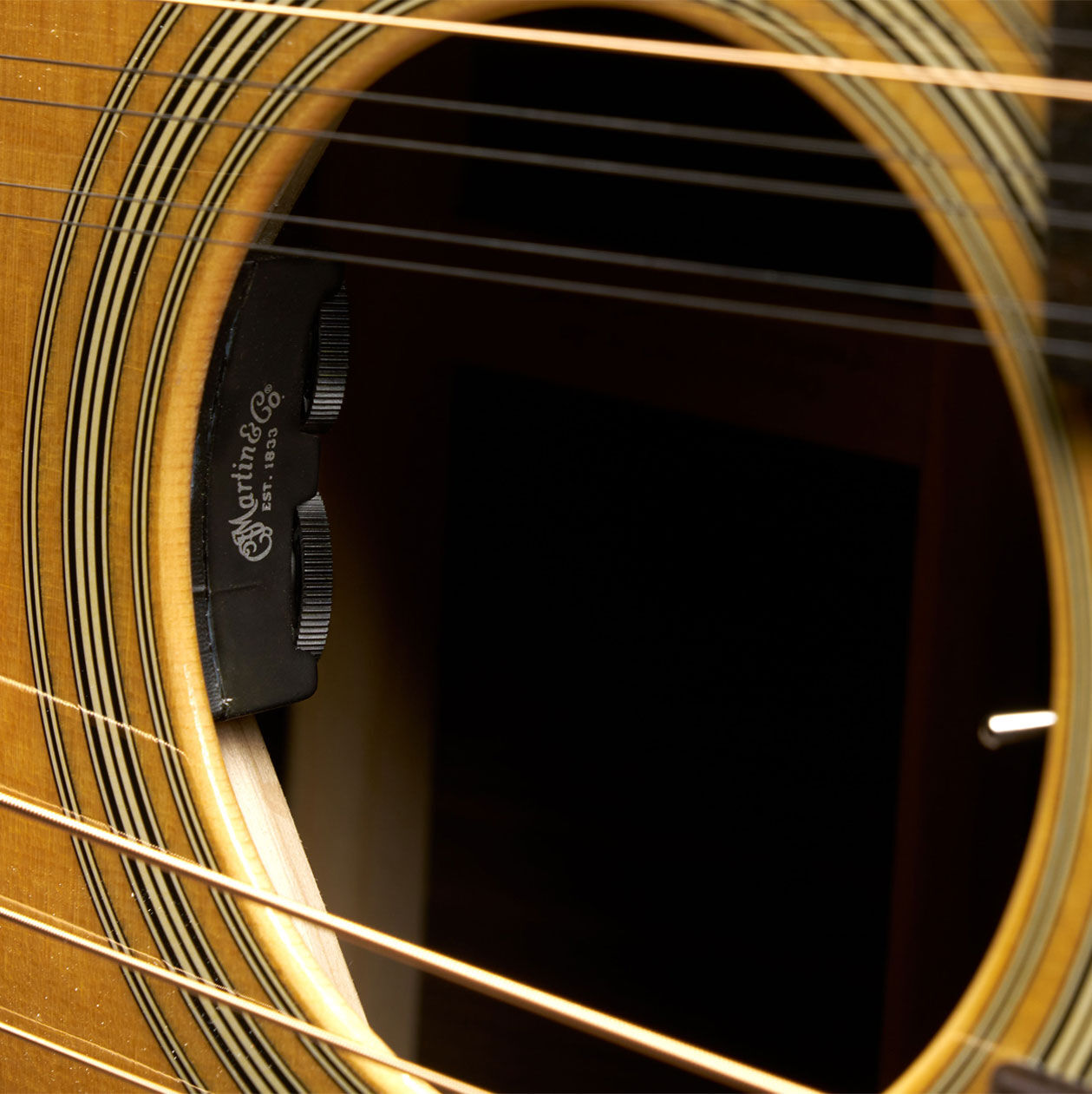 Closeup shot of the sound hole, with the two separate sets of strings crossing the body of the Grand J-28E DN