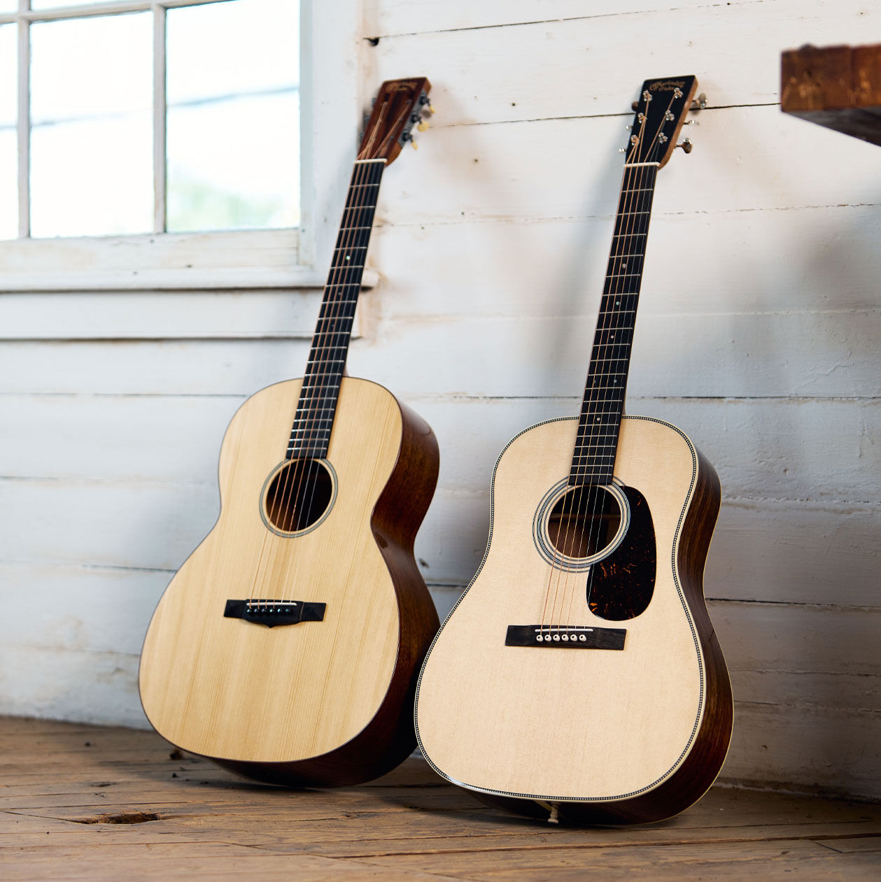 Two acoustic guitars leaning against a white wall