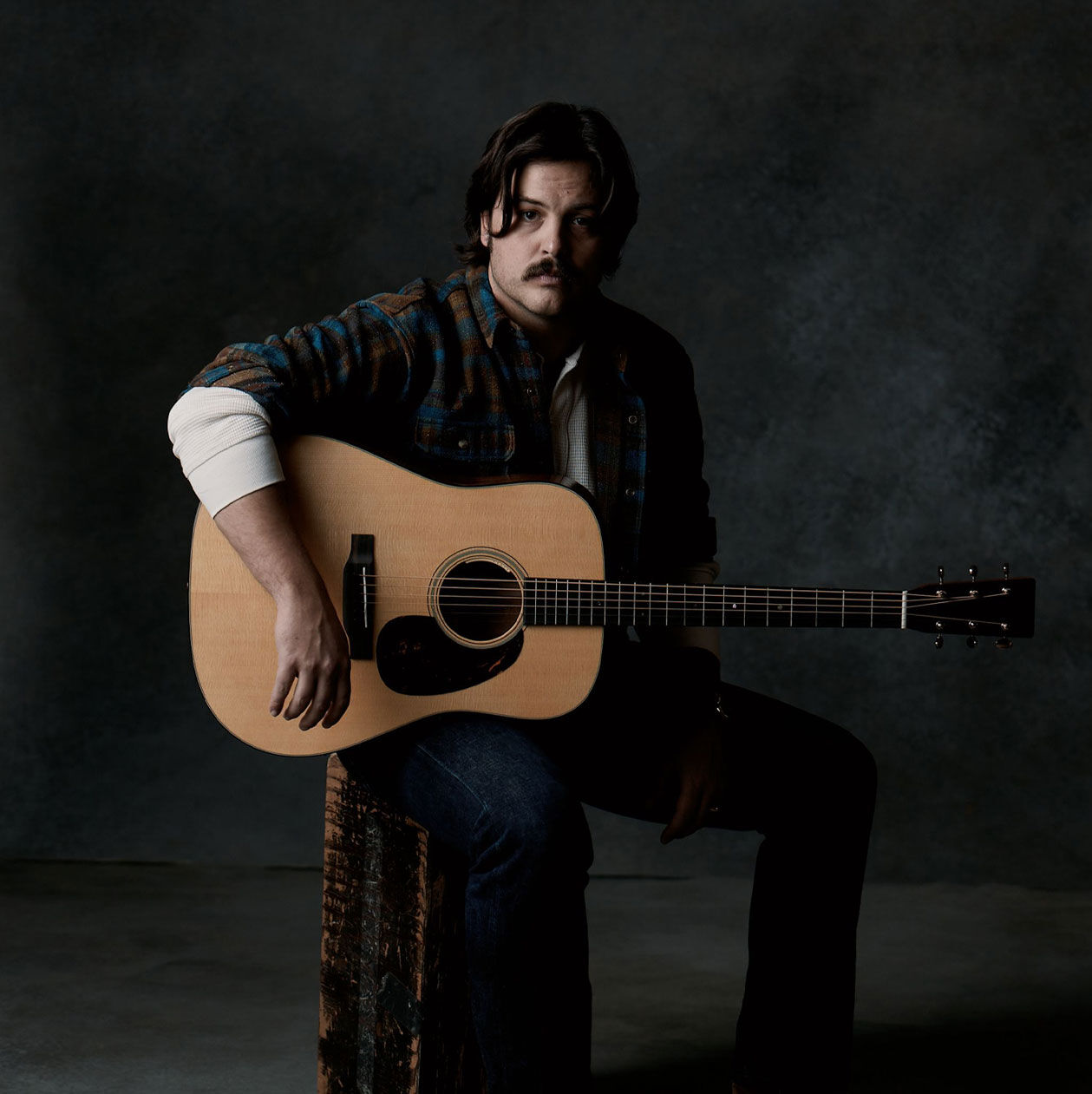 Photo of JD Clayton clad in dark denim holding an acoustic guitar