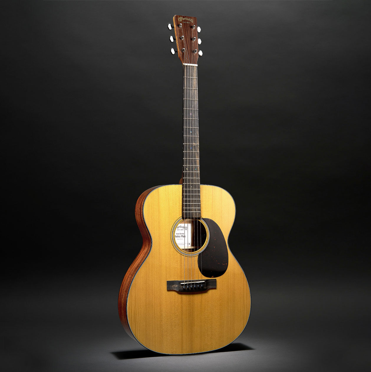 The 000E Retro Plus Mahogany acoustic guitar on a black background