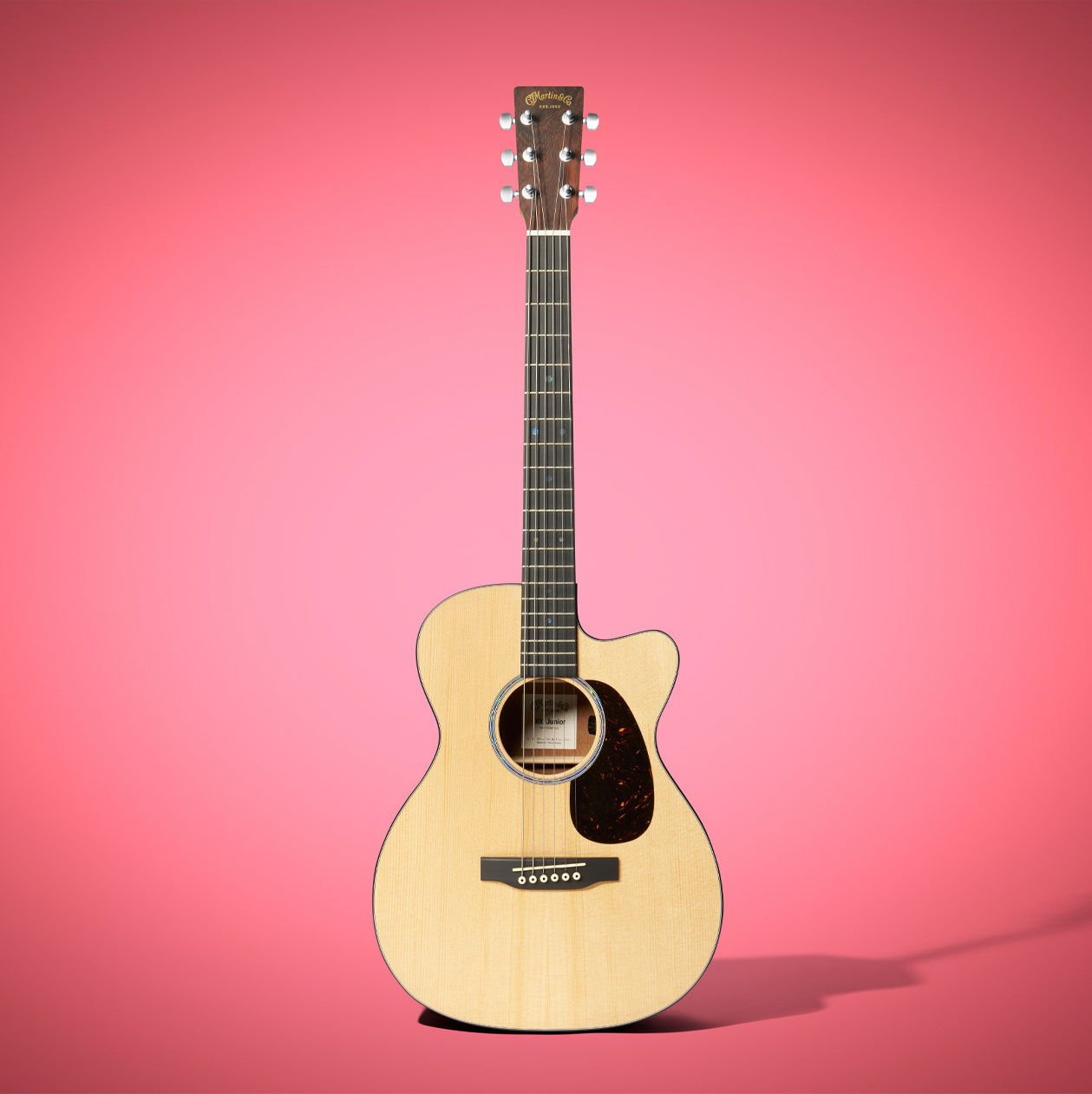The 000C Jr E cutaway guitar on a pink background
