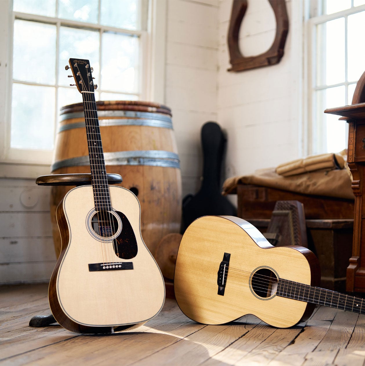 Two guitars, one standing up, one layind down on hardwood floor.